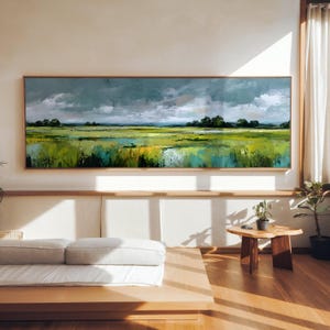 Peut inclure: Une peinture de paysage panoramique représentant une prairie aux tons vert et jaune vifs sous un ciel gris orageux et dramatique. L'œuvre est encadrée d'une fine bordure en bois et montre un horizon plat avec des arbres au loin.