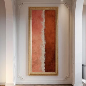 Peut inclure: Un grand tableau abstrait rectangulaire avec un cadre doré. L'œuvre présente une division verticale, avec le côté gauche dans des tons roses et le côté droit dans des tons rouge-brun. Une bande verticale blanche divise les deux couleurs. Le tableau est accroché sur un mur blanc.