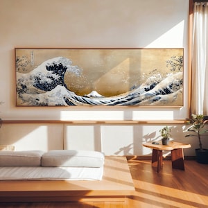 May include: A framed print of Hokusai's "The Great Wave off Kanagawa" features a large, stylized wave in shades of blue and white, with Mount Fuji in the background. The artwork is set against a tan backdrop and framed in a natural wood tone.