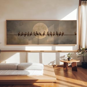 Peut inclure: Une œuvre d'art encadrée représente des oiseaux perchés sur un fil, devant un fond de pleine lune et de ciel nuageux. L'œuvre est exposée au-dessus d'une plateforme en bois avec un matelas blanc et une petite table en bois.