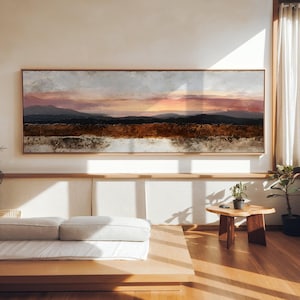 Peut inclure: Une peinture de paysage panoramique dans un cadre en bois fin représentant un ciel au coucher du soleil avec des teintes roses et orange au-dessus de silhouettes de montagnes sombres et un premier plan texturé brun terreux.