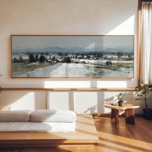 Peut inclure: Une grande peinture de paysage encadrée de bois représente une vallée avec une rivière et des montagnes lointaines. L'œuvre utilise une palette de gris, de verts et de blancs, créant une atmosphère calme. Le tableau est accroché au-dessus d'une plateforme en bois avec un matelas blanc.