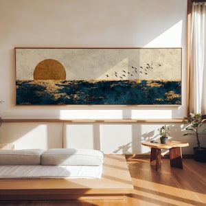 Puede incluir: Una gran obra de arte rectangular en lienzo que representa una puesta de sol sobre el océano. La obra presenta un sol dorado, olas azul oscuro con detalles dorados y una bandada de pájaros. Enmarcada en un marco de madera marrón claro.