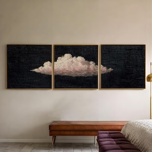Op de afbeelding: Driedelige set ingelijste kunst met een wolkenformatie. Elk stuk heeft een donkere achtergrond met een gouden lijst. De wolk is geschilderd in roze en wit, wat een opvallend contrast creëert. Het kunstwerk wordt tentoongesteld boven een bruine bank.