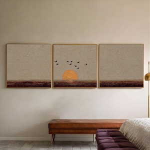 Peut inclure: Un triptyque d'art mural encadré représentant un coucher de soleil. L'œuvre d'art représente un grand soleil orange se couchant sur un horizon brun foncé, avec des oiseaux noirs volant au-dessus. Le fond est beige texturé, et les cadres sont dorés.