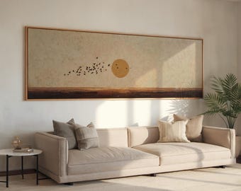 May include: A beige sectional sofa with decorative pillows sits below a large framed landscape painting. The artwork depicts a sunset with a golden sun, a flock of birds, and a brown horizon line. A small side table and a potted plant are also visible.