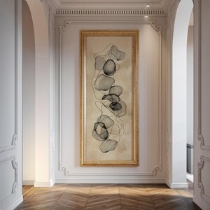 Könnte beinhalten: Vertikal gerahmtes Kunstwerk mit einem abstrakten Design aus miteinander verbundenen, organischen Formen in Grau- und Schwarztönen. Das Kunstwerk ist vor einem beigefarbenen Hintergrund platziert und goldfarben gerahmt, was dem Innenraum Eleganz verleiht.