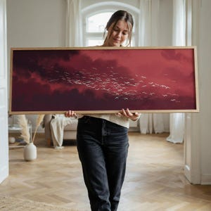 Peut inclure: Une œuvre d'art murale rectangulaire présentant une peinture de paysage panoramique d'un grand groupe d'oiseaux blancs volant à travers un ciel nuageux rouge profond et bordeaux foncé, encadrée dans un cadre en bois clair aux bords simples.