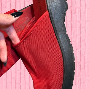 Pode incluir: Sandálias de plataforma vermelhas com sola preta. As sandálias têm uma parte superior de tecido vermelho texturizado e uma sola preta grossa. A imagem mostra um close-up da sandália, destacando os materiais e o design.