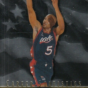 Puede incluir: Tarjeta de baloncesto con un jugador con la camiseta de USA, número 5. Fondo oscuro con logo de USA Basketball y texto "Career Statistics". El jugador está en pleno lanzamiento, con los brazos extendidos. Borde dorado.