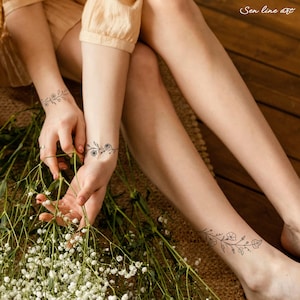 Puede incluir: Dos tatuajes temporales de enredaderas florales con peque&ntilde;as flores en el brazo y el tobillo de una persona. Los tatuajes son en blanco y negro y est&aacute;n en la piel de una persona.