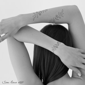 Puede incluir: Una imagen en blanco y negro de un brazo con un tatuaje simple de l&iacute;nea de arte de un dise&ntilde;o floral. El tatuaje est&aacute; en la mu&ntilde;eca y el antebrazo.