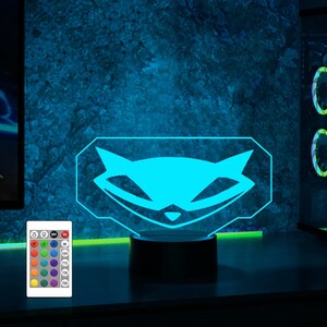 May include: A blue and white 3D printed night light shaped like the logo for the video game "The Stanley Parable". The light is on a black base and has a remote control with multiple colour options.