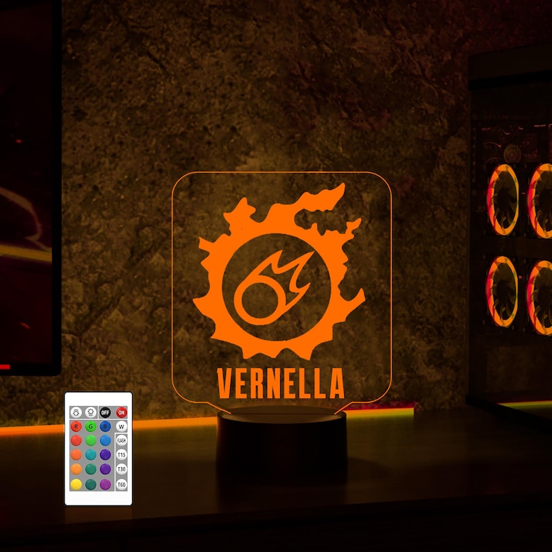 May include: Orange illuminated acrylic sign featuring a stylised fire symbol and the name "VERNELLA" underneath. The sign is mounted on a black base and is lit with a multi-coloured LED light. A remote control with various colour options is also pictured.