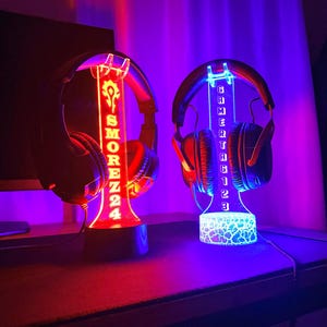 May include: Two illuminated headphone stands with custom engraved names. The stand on the left is red and says "SMOREZZ24". The stand on the right is blue and says "GAMERTHG123".