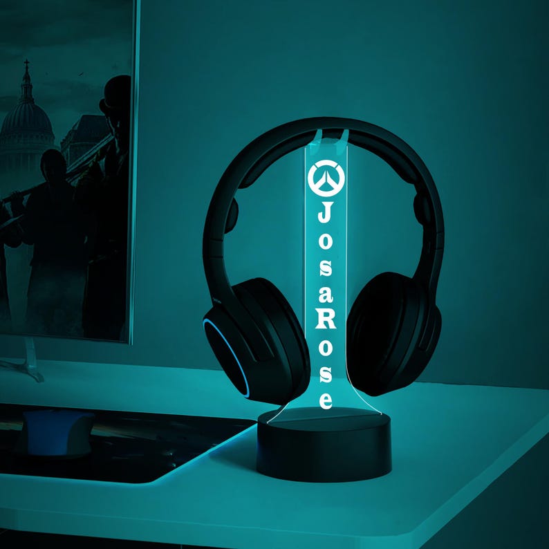 May include: A blue and white LED light with a gamer logo and the name "JosaRose" on it. The light is on a black base and has a pair of black headphones resting on it.