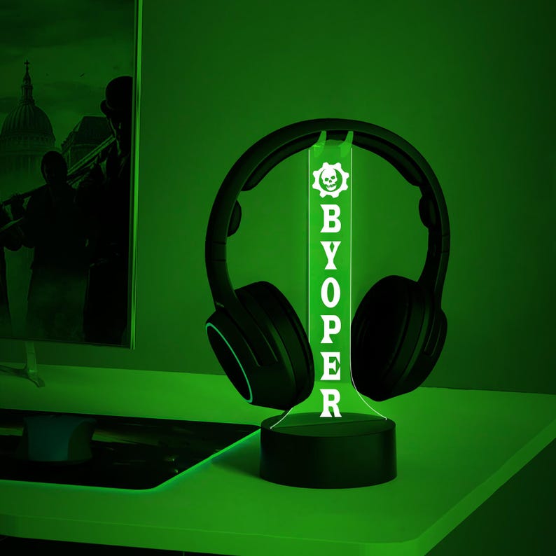 Op de afbeelding: Een groen LED-licht met een schedel en gekruiste beenderen afbeelding en de tekst "BYOPER" op een zwarte basis. Een zwarte koptelefoon rust op het licht.