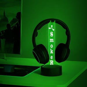 May include: A green LED light with a black base and a pair of black headphones on top. The light has the word "SMOKER" written on it.