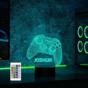 May include: A green and black 3D printed gamer controller night light with the name "Joshua" on the base. The light is on a black base and has a remote control with multiple color options.