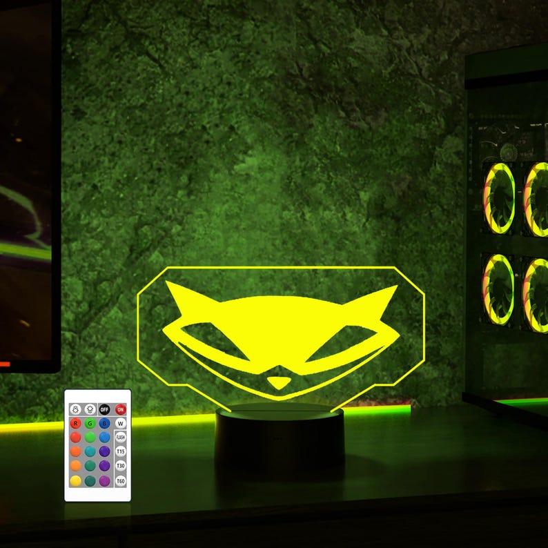 May include: A yellow raccoon logo illuminated on a black base with a remote control for changing the color of the light. The logo is a stylized raccoon face with a mischievous grin.