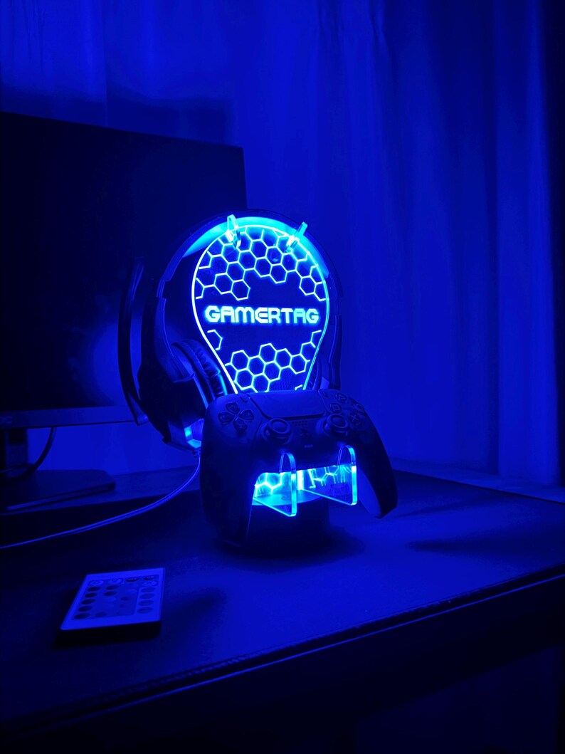 May include: A blue LED light stand with a honeycomb design and the word "GAMERTAG" in white. The stand holds a black video game controller.