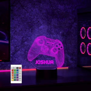 May include: A purple 3D printed gamer controller night light with the name "Joshua" printed below it. The light is on a black base and is illuminated with a purple glow. A remote control with multiple color options is included.