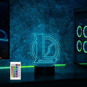 May include: A blue and white 3D printed LED night light with the text "JAMOLOGGA" on the base. The light is on a black base and has a remote control with multiple color options.