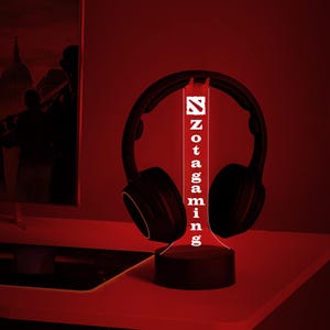 May include: A black and white 3D printed lamp with the word "Zotac Gaming" printed vertically on the front. The lamp is lit up in red and is sitting on a black base. A pair of black headphones are resting on the top of the lamp.