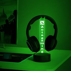 May include: A green illuminated Zotac Gaming logo on a black stand with a pair of black headphones resting on the stand.