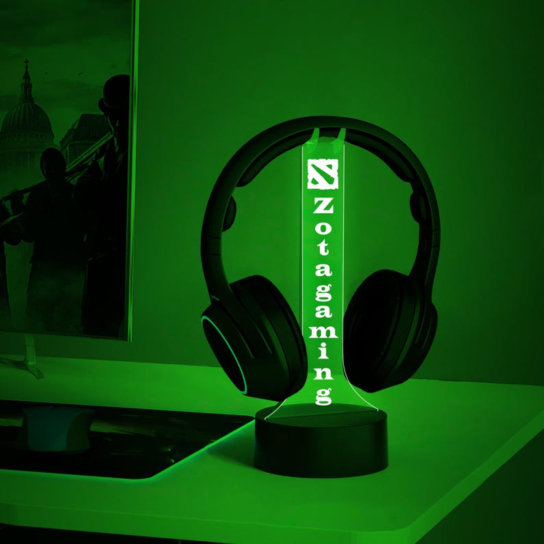 May include: A green illuminated Zotac Gaming logo on a black stand with a pair of black headphones resting on the stand.