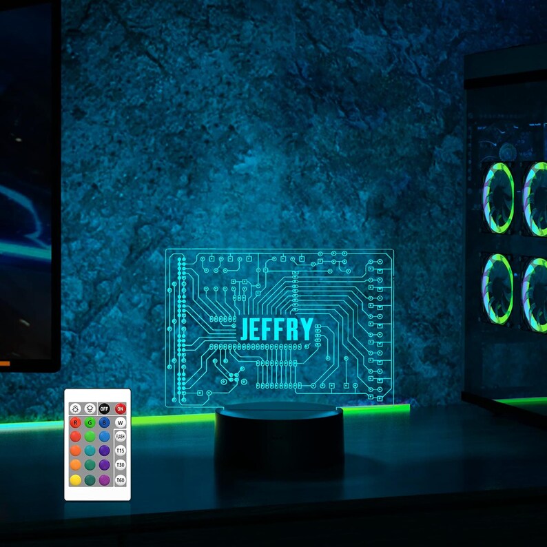 K&ouml;nnte beinhalten: Ein Nachtlicht mit einem blauen und gr&uuml;nen Design einer Leiterplatte mit dem Namen "JEFFRY" in der Mitte. Das Licht steht auf einem schwarzen Sockel und hat eine Fernbedienung mit mehreren Farboptionen.