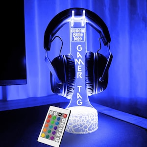 May include: A white LED light stand with a gamer tag inscription and a headset holder. The stand has a textured base and is illuminated with a blue light. A remote control with color options is included.