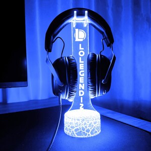 May include: A glowing blue headphone stand with the text "LOLENDIN" vertically displayed. The stand holds a pair of black headphones. The base of the stand has a cracked pattern design, and the background is a gradient of blue.