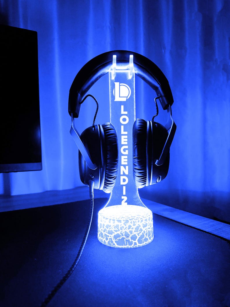 May include: A glowing blue headphone stand with the text "LOLENDIN" vertically displayed. The stand holds a pair of black headphones. The base of the stand has a cracked pattern design, and the background is a gradient of blue.
