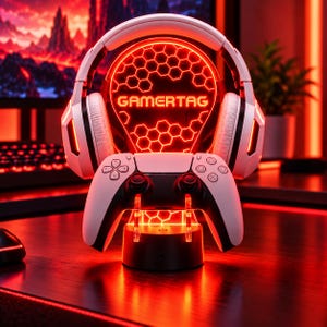 Puede incluir: Unos auriculares de juego blancos y un mando inalámbrico blanco sobre un soporte circular. El soporte cuenta con un panel de luz circular rojo brillante con un patrón de panal y el texto GAMERTAG impreso en el centro en negrita.