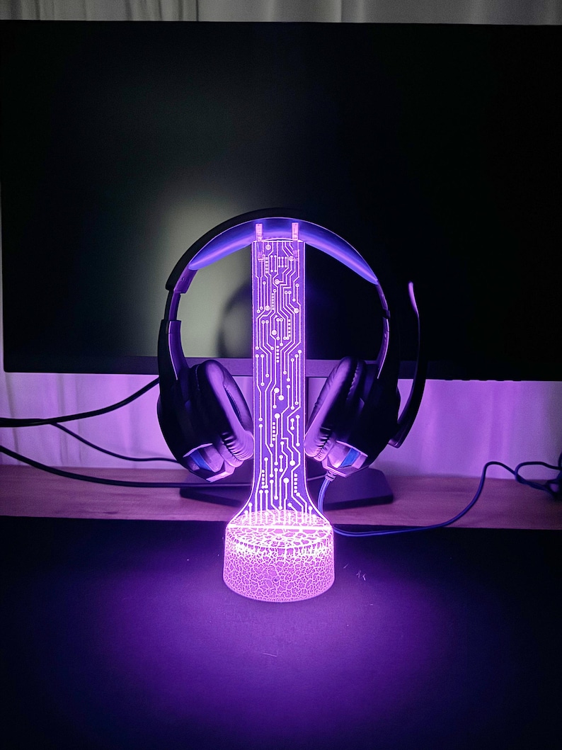 Op de afbeelding: Een paarse LED-lamp met een printplaatontwerp houdt een zwarte koptelefoon vast. De lamp heeft een getextureerde basis.