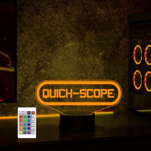 May include: A 3D printed orange neon sign with the text "QUICK-SCOPE" on a black base. The sign is illuminated and has a remote control with multiple color options.
