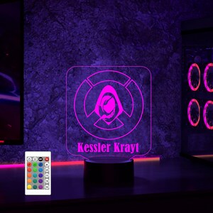 May include: A purple and white LED night light with a hooded figure design and the name "Kessler Krayt" printed below. The light is on a black base and has a remote control with multiple color options.
