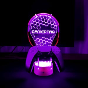 May include: A purple and white LED light with a honeycomb design and the word "GAMERTAG" in white. The light is mounted on a black controller.