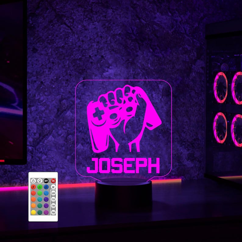 May include: A pink LED night light with a gamer controller design and the name "JOSEPH" printed below. The light is on a black base and has a remote control with multiple color options.