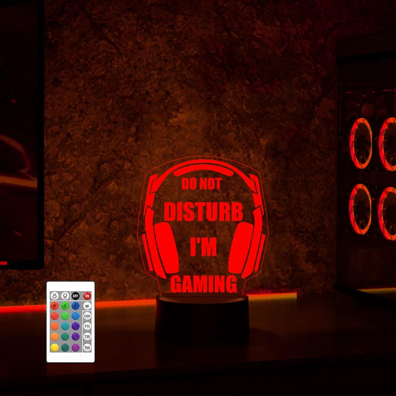 Puede incluir: Una luz nocturna LED roja con auriculares para juegos y el texto "No molestar, estoy jugando". La luz tiene un control remoto con m&uacute;ltiples opciones de color.