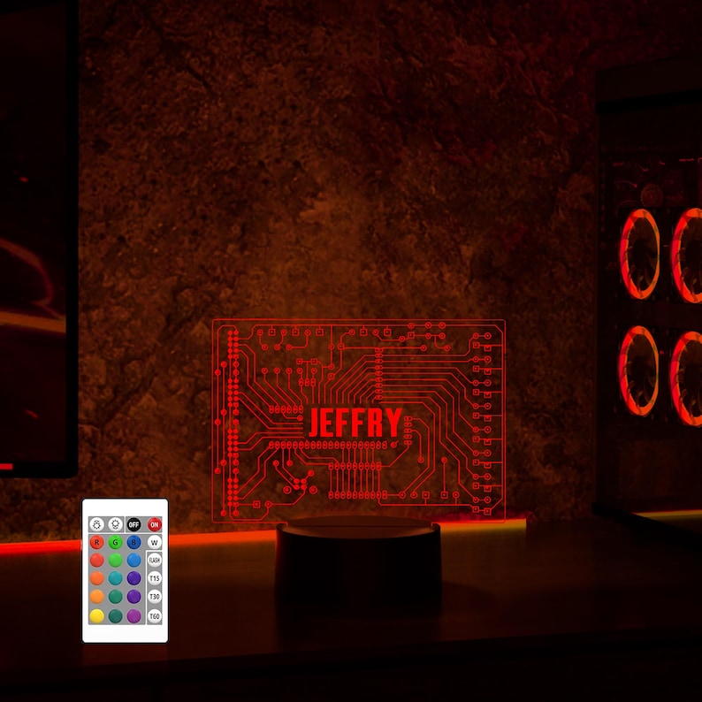 K&ouml;nnte beinhalten: Ein rotes LED-Nachtlicht mit einem Schaltkreisdesign und dem Namen "JEFFRY" darauf gedruckt. Das Licht steht auf einem runden Sockel und leuchtet rot. Eine Fernbedienung mit mehreren Farboptionen ist ebenfalls abgebildet.