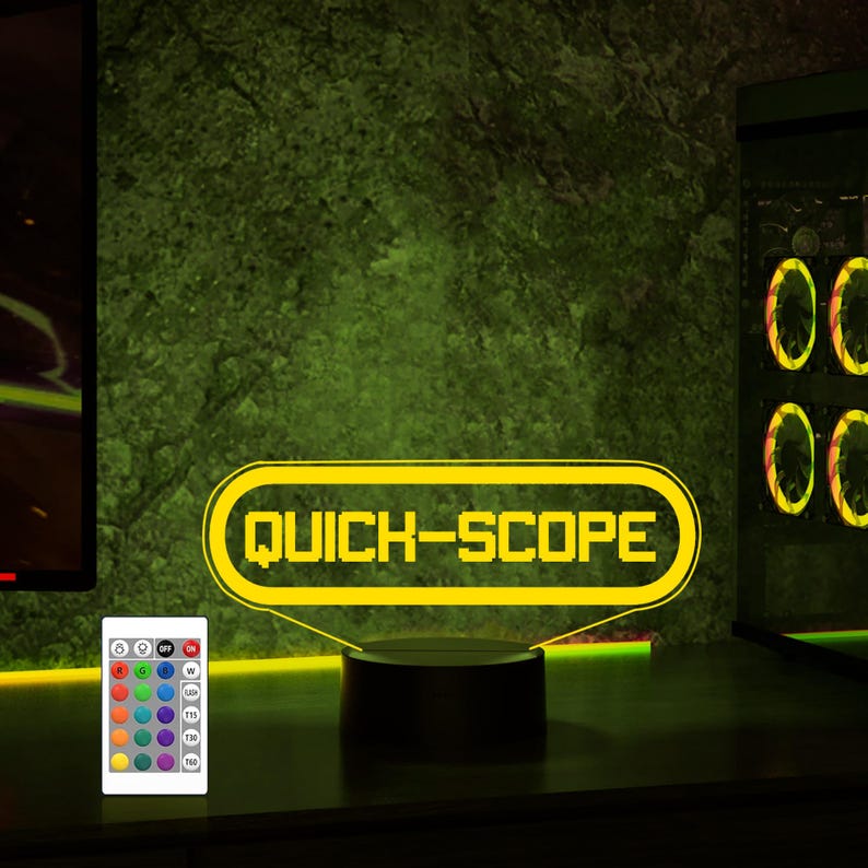 May include: A yellow neon sign with the text "QUICK-SCOPE" in a retro video game style. The sign is on a black base and has a remote control with multiple colored lights.