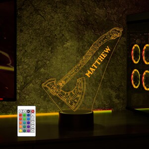 May include: A 3D printed night light shaped like an axe with intricate details and a personalized name "MATTHEW". The light is illuminated in a warm yellow color and has a remote control with multiple color options.