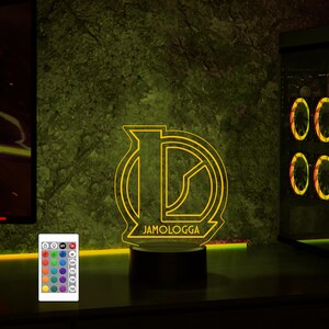 May include: A yellow LED night light with a custom logo that says "JAMOLOGGA". The light is on a black base and has a remote control with multiple color options.