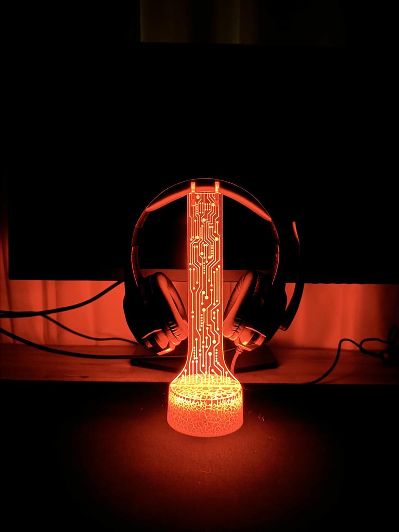 Op de afbeelding: Een rood LED-licht met een printplaatontwerp, gevormd als een standaard voor koptelefoons. Het licht is aan en verlicht de koptelefoons.