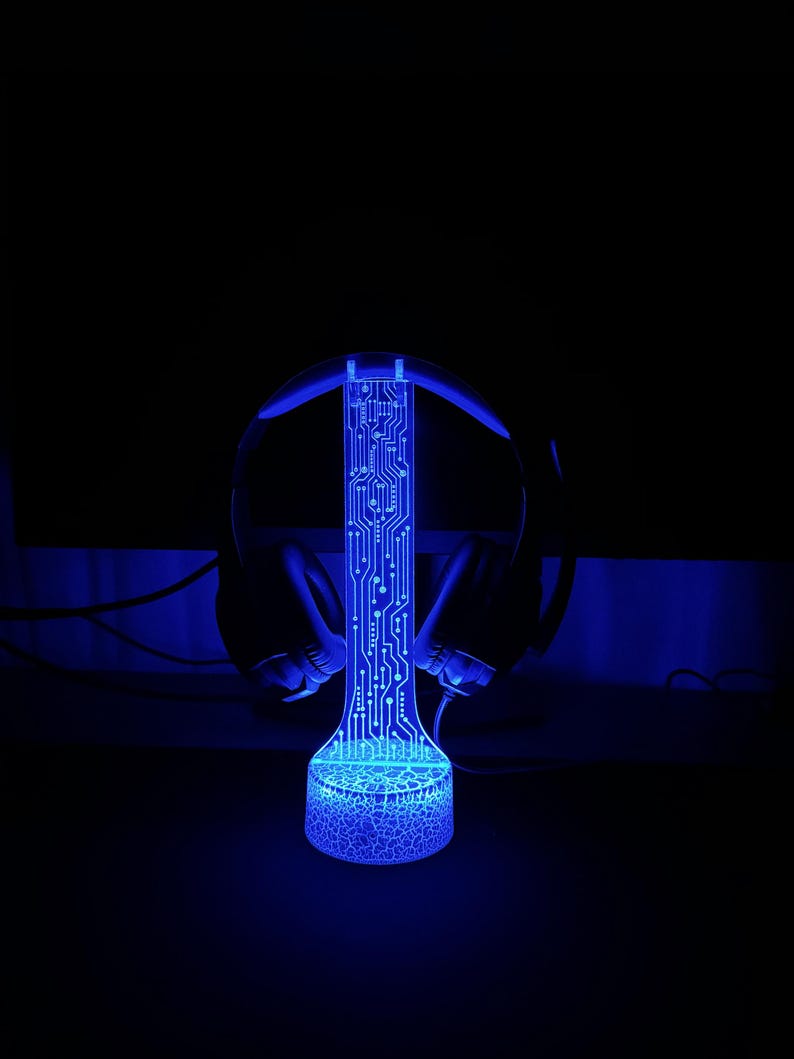Puede incluir: Una luz LED azul con un dise&ntilde;o de placa de circuito, con forma de cilindro alto, con unos auriculares negros apoyados en la parte superior.