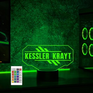 Pu&ograve; includere: Una luce LED verde con un design personalizzato che presenta il testo "Kessler Krayt". La luce &egrave; su una base nera e ha un telecomando con pi&ugrave; opzioni di colore.