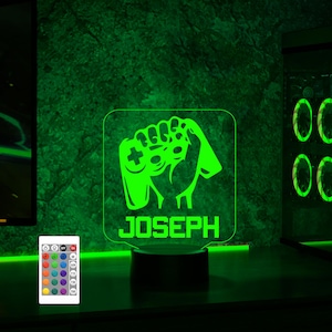 May include: Green LED night light with a gamer hand holding a controller and the name "JOSEPH" below. The light is on a black base and comes with a remote control.