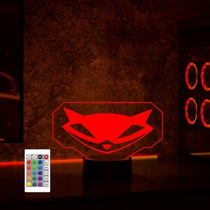 May include: A red LED night light shaped like the logo for the video game "Sly Cooper". The light is on a black base and has a remote control with multiple color options.